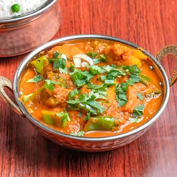 Everest Indian Kitchen's vibrant orange curry with green peppers and cilantro, served in a metal bowl.