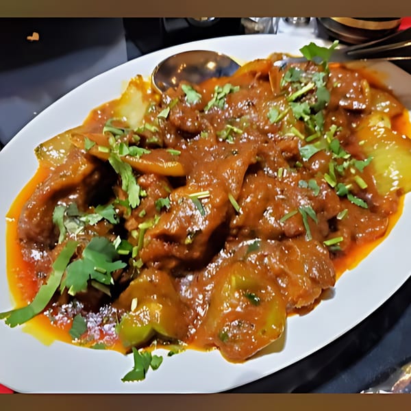A white oval plate filled with a rich, reddish-brown Indian curry, garnished with fresh cilantro.