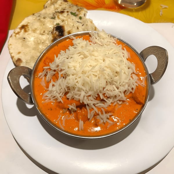 Everest Indian Kitchen's butter chicken with rice in a metal bowl, served with naan bread.